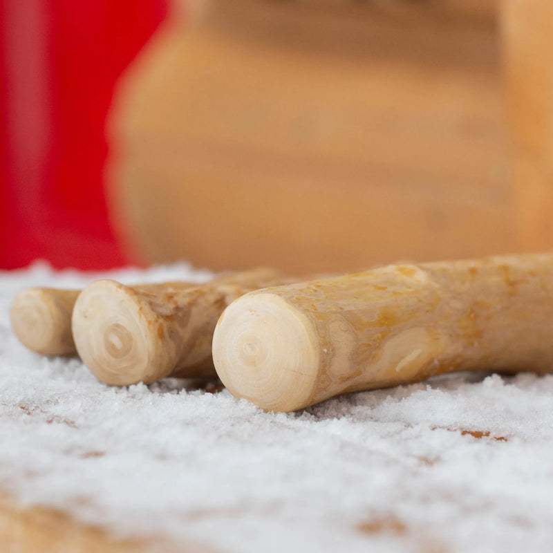 Gros plan de trois bâtons à mâcher en bois de caféier Mes Biscuits Maison déposés dans la neige